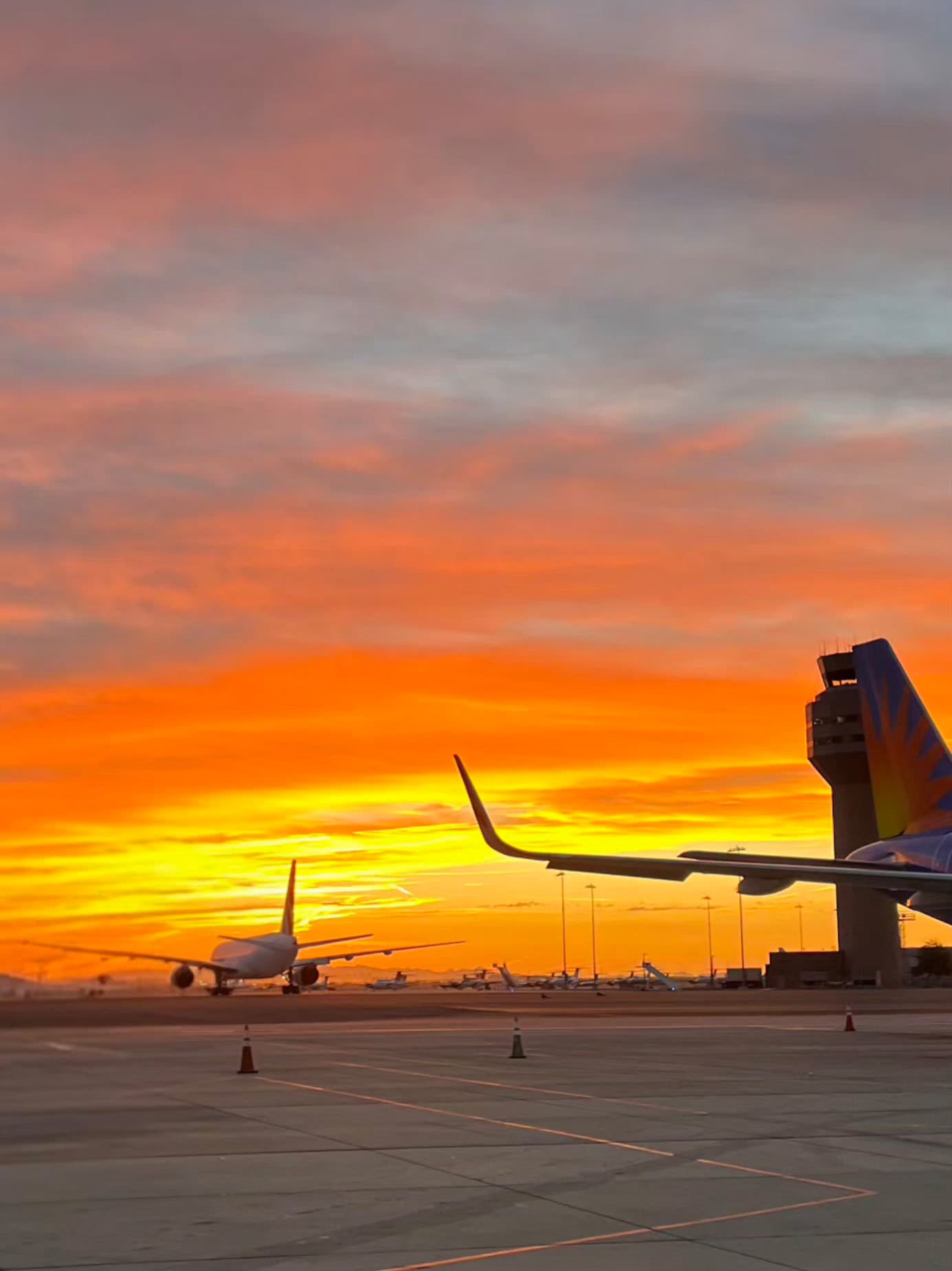 A spectacular fiery sunset transforms the mundane airport tarmac into a dramatic stage where commercial aviation meets nature's daily theater.