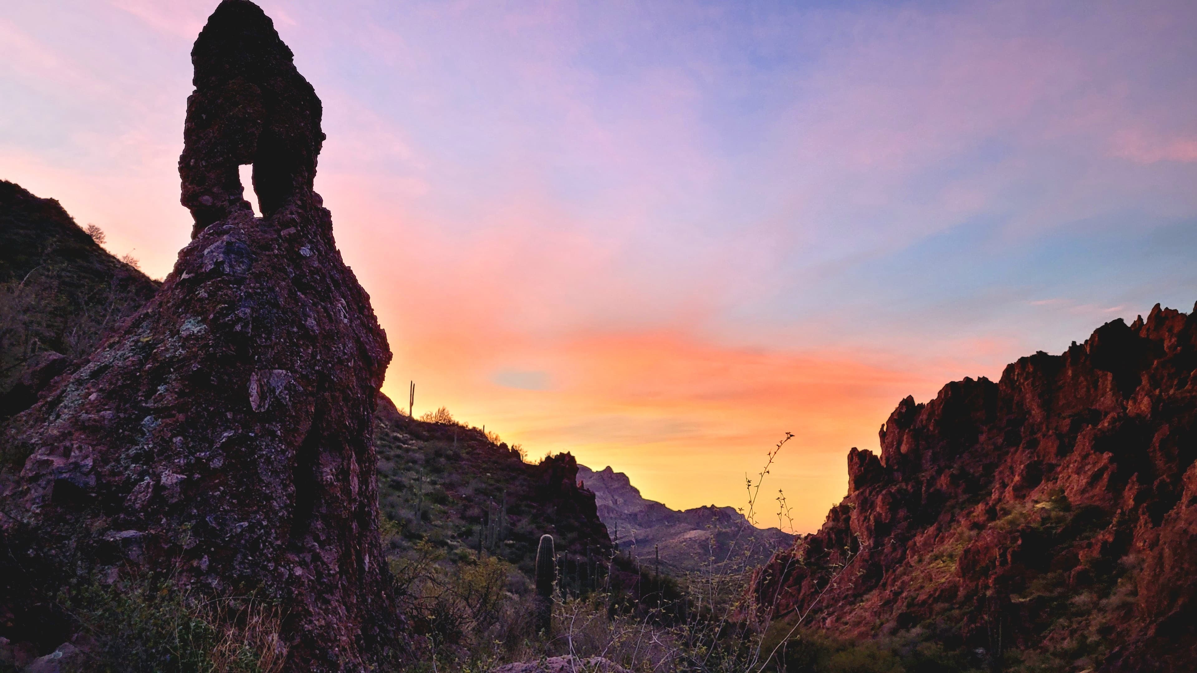 A mystical desert dawn where ancient rock formations stand sentinel against a canvas of purple and gold light.