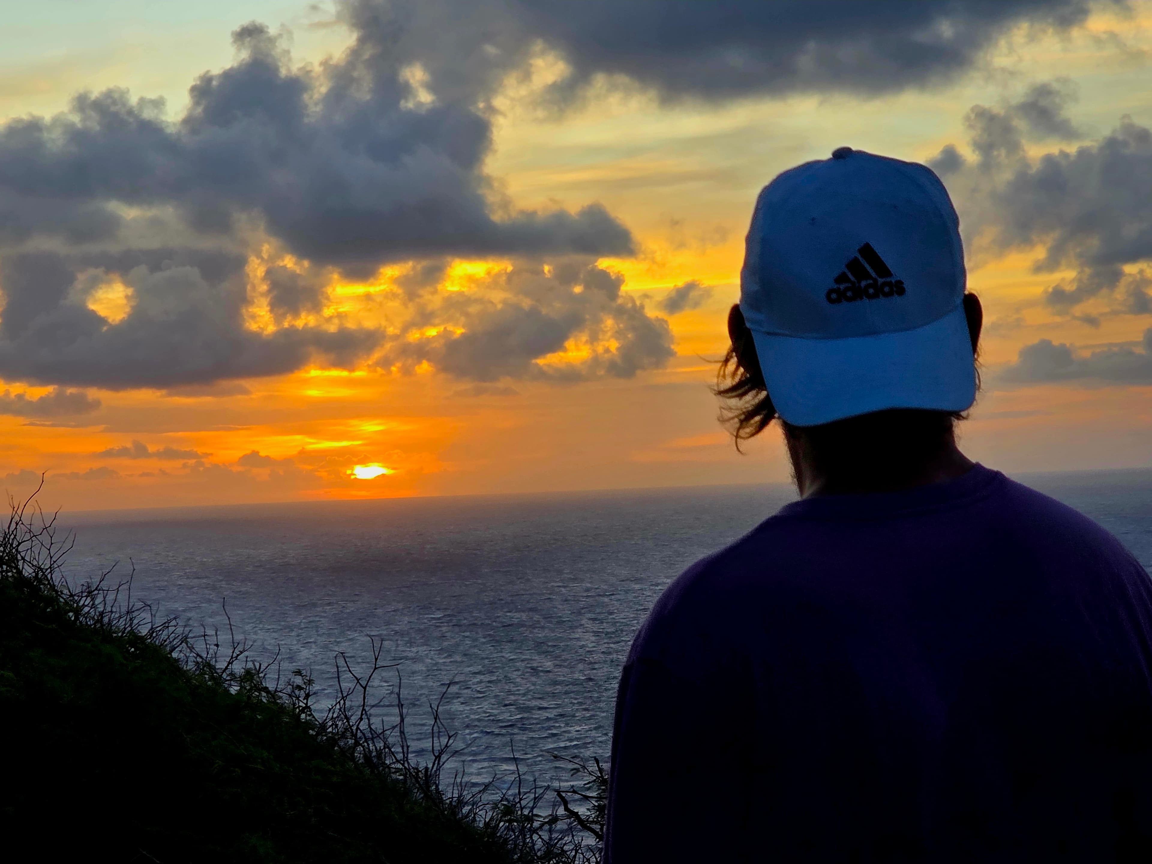 A contemplative moment where golden storm light breaks through dramatic clouds over the endless ocean, witnessed in peaceful solitude.