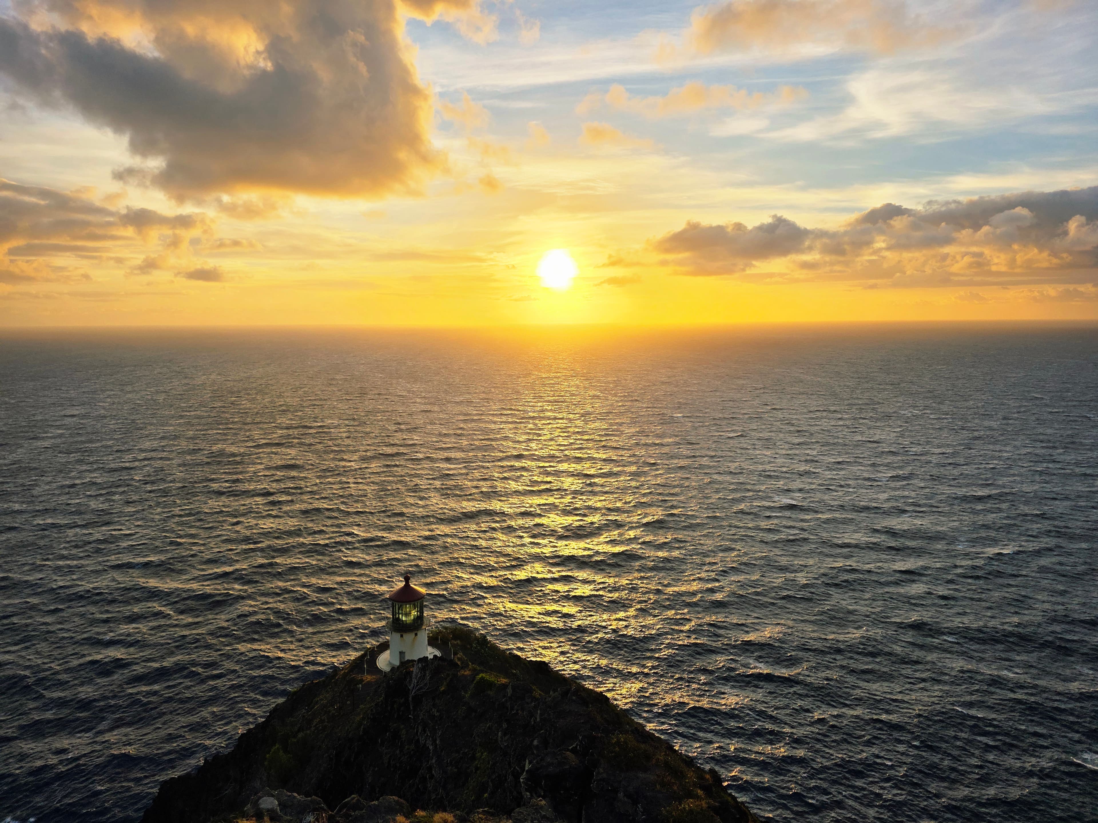 A beacon of hope stands sentinel against the golden Pacific dawn, where dramatic clouds dance with brilliant sunrise colors over endless ocean.