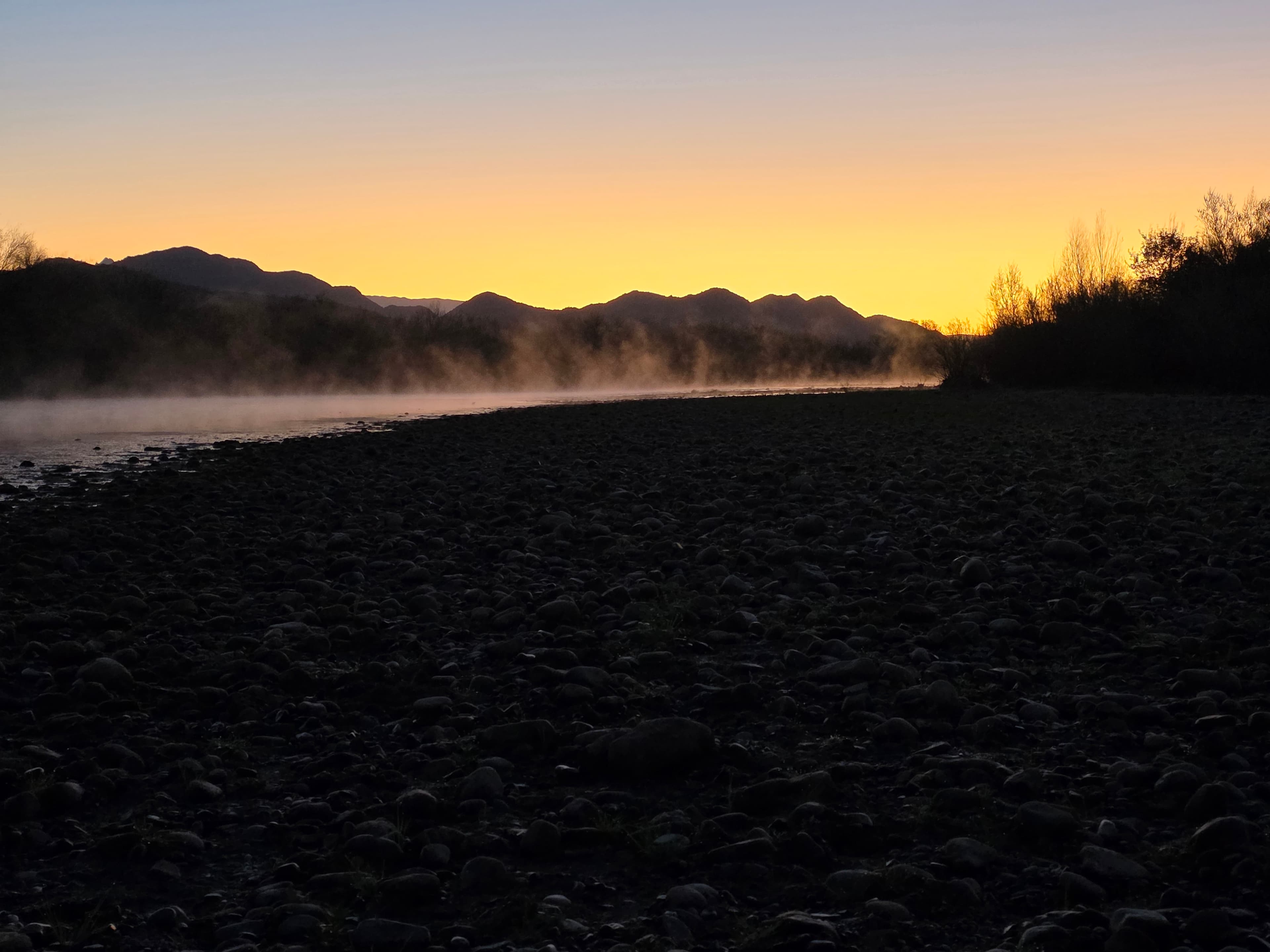 A serene mountain dawn where rising mist dances above still waters, creating an ethereal boundary between earth and sky.
