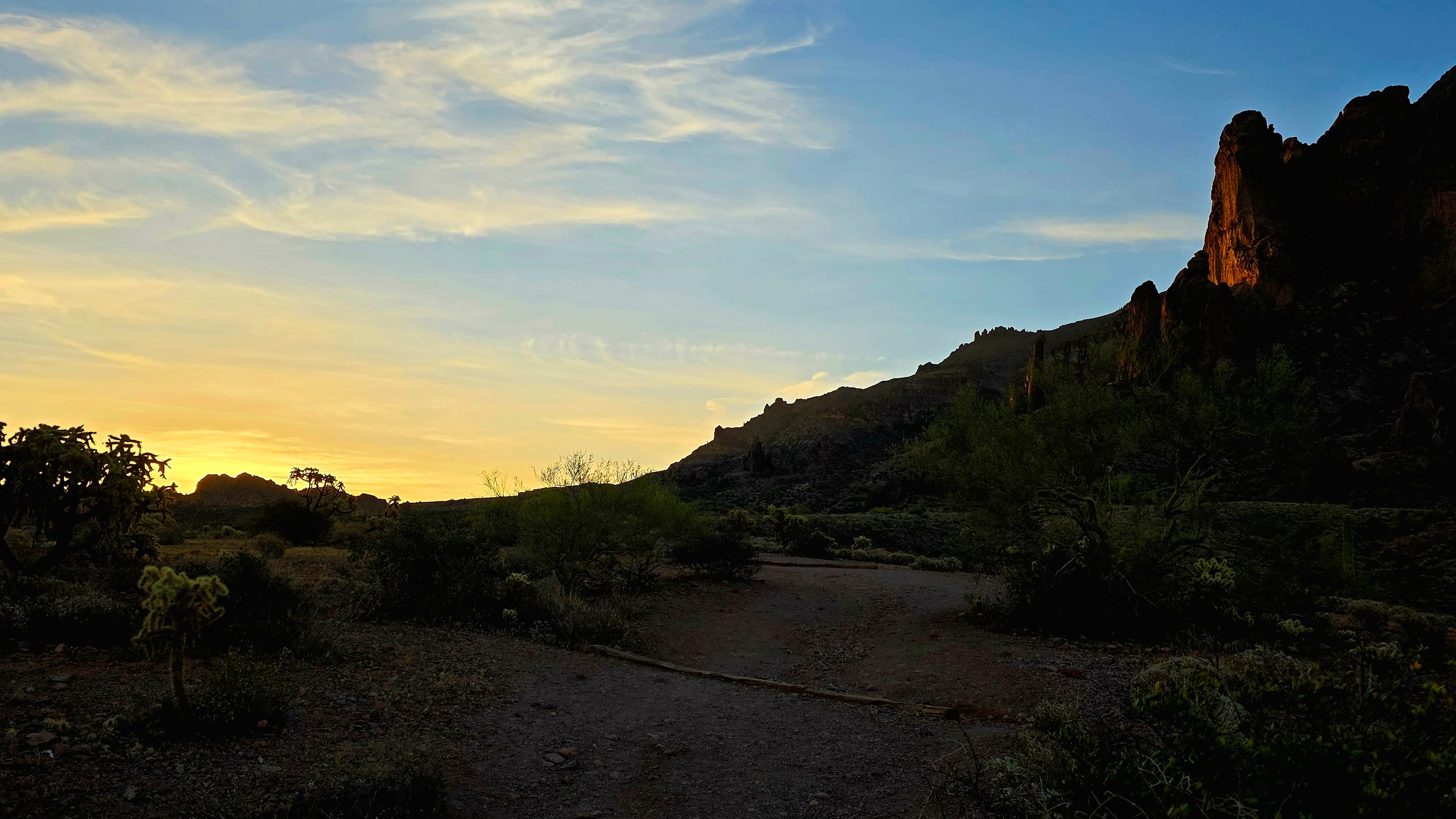 A serene desert dawn unfolds along a winding trail, where soft golden light kisses ancient rock formations in peaceful solitude.