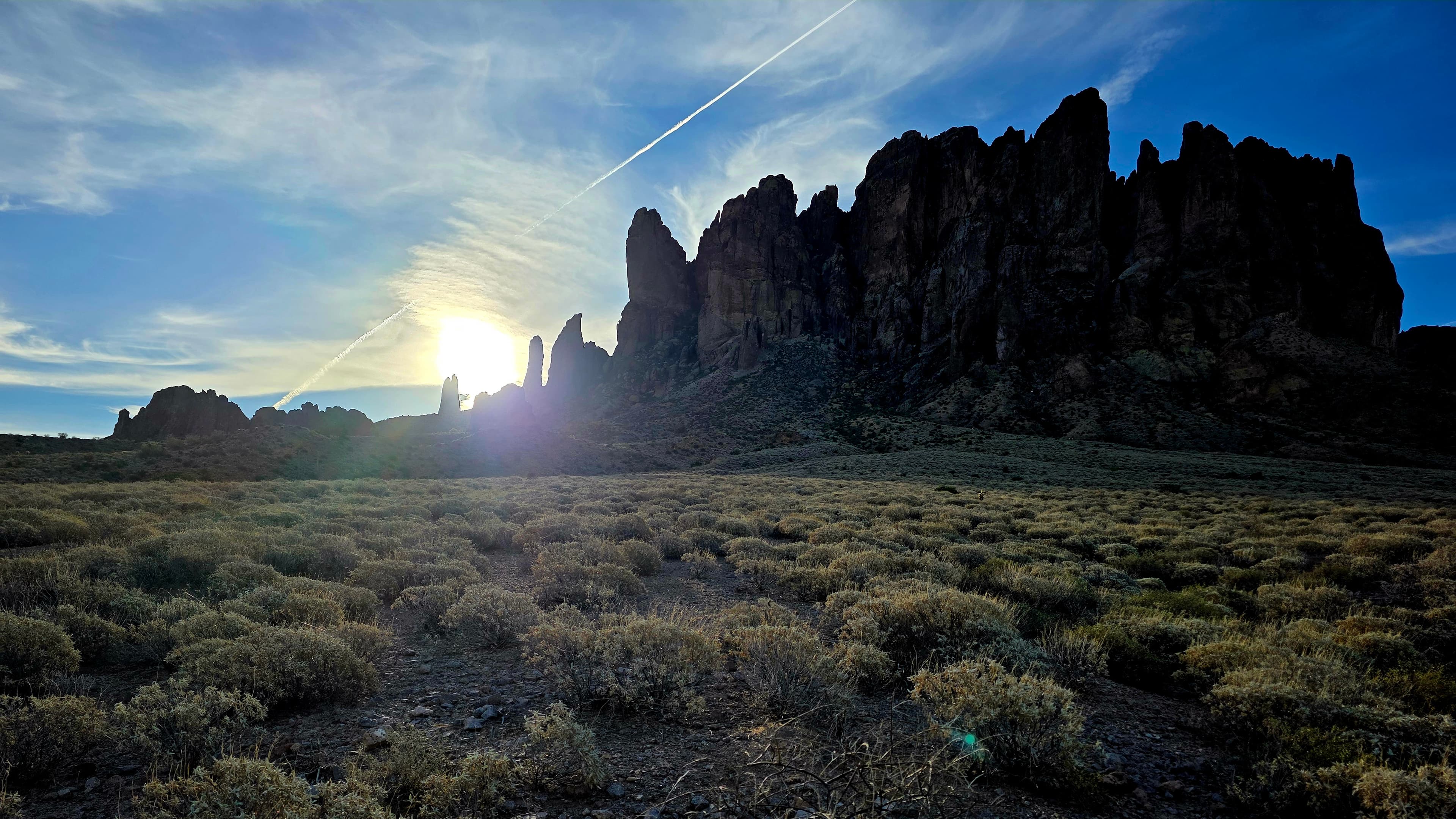 A dramatic desert sunrise pierces through towering rock spires, casting ethereal light across the rugged wilderness landscape.