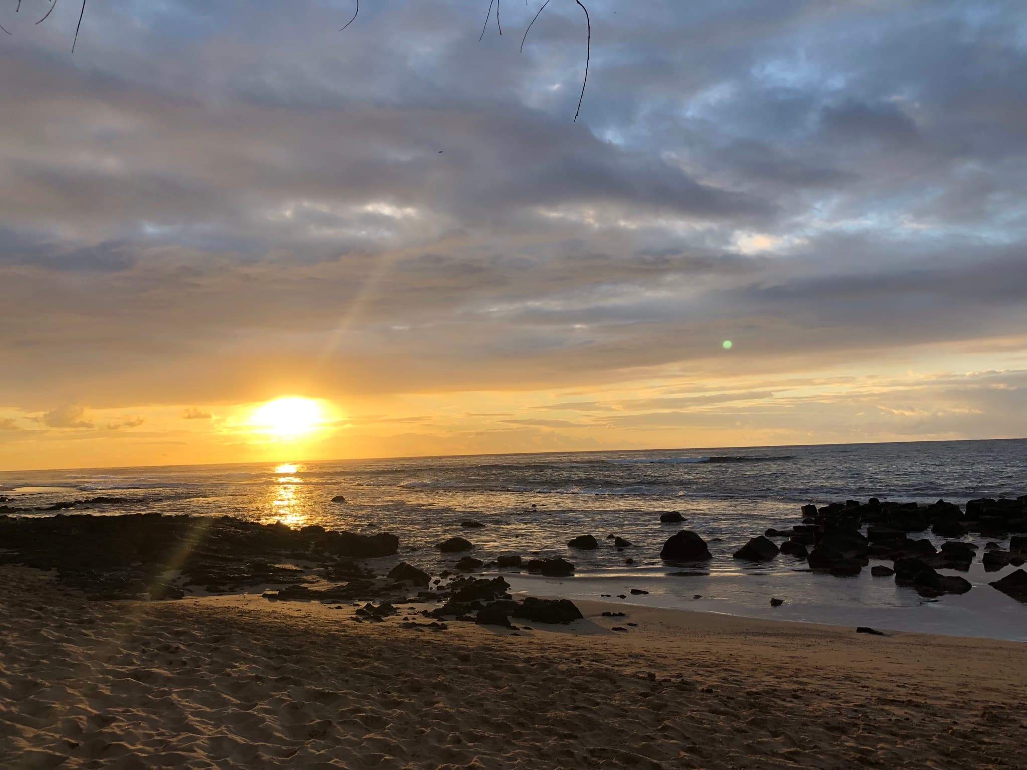 A serene coastal sunrise with golden warmth breaking through moody clouds over a rocky shoreline.